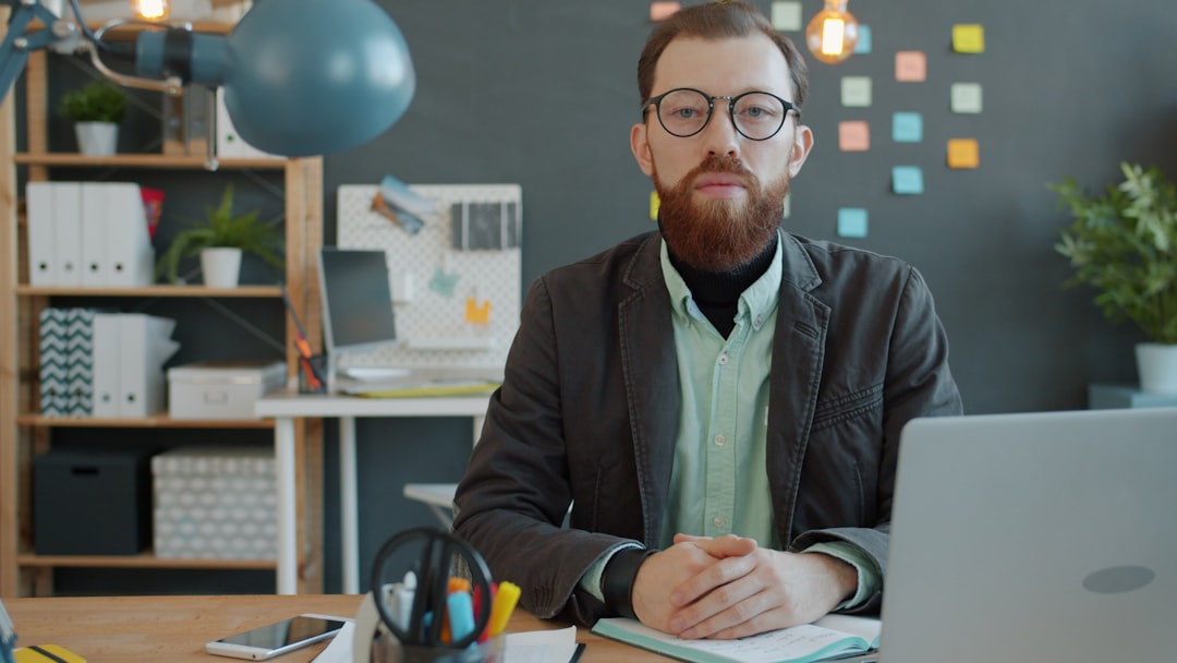 Man with beard and glasses sitting at desk.
